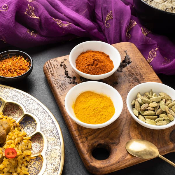 Indian spices: saffron, turmeric, paprika, and cardamom pods, with biryani on a decorative plate.
