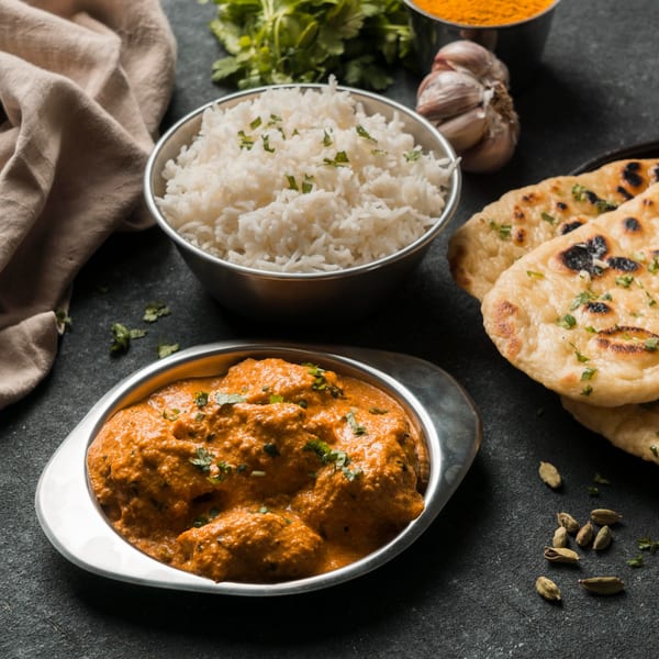Indian butter chicken, rice, and naan bread with spices and herbs on a dark surface.