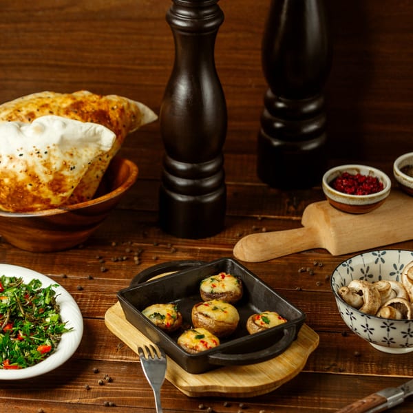 Indian stuffed mushrooms in a cast iron pan, with naan bread, salad, and spices on a wooden table.