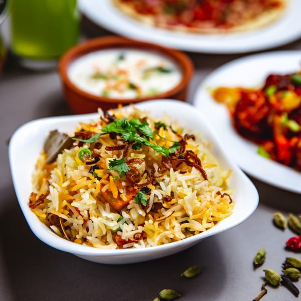 Close-up of Indian biryani rice with cilantro, fried onions, and spices, with other dishes blurred in background.
