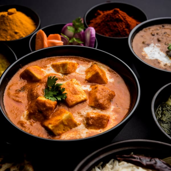 Close-up of Indian paneer butter masala, dal makhani, and other dishes with spices.
